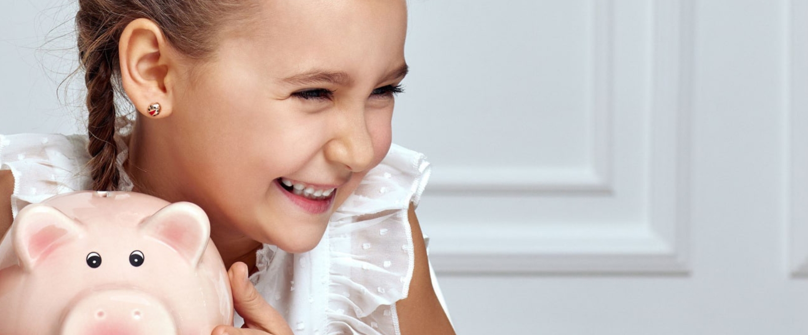 A young girl smiles brightly as she shakes her pink piggy bank