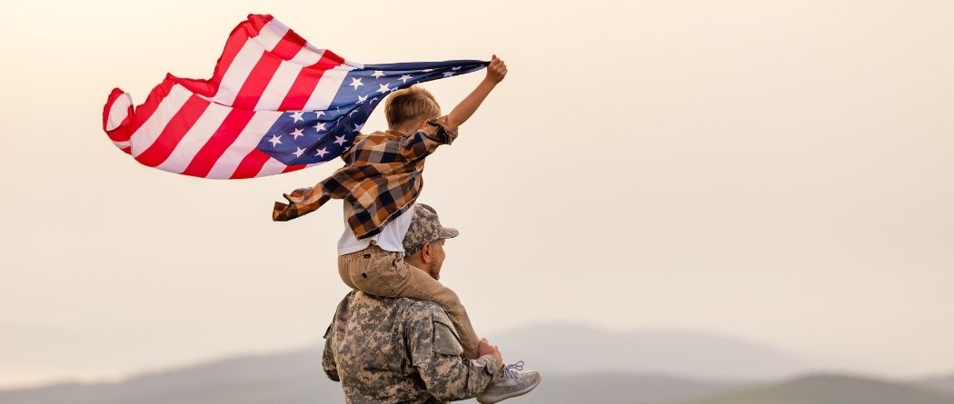 Little boy on military man's shoulders holding an American flag