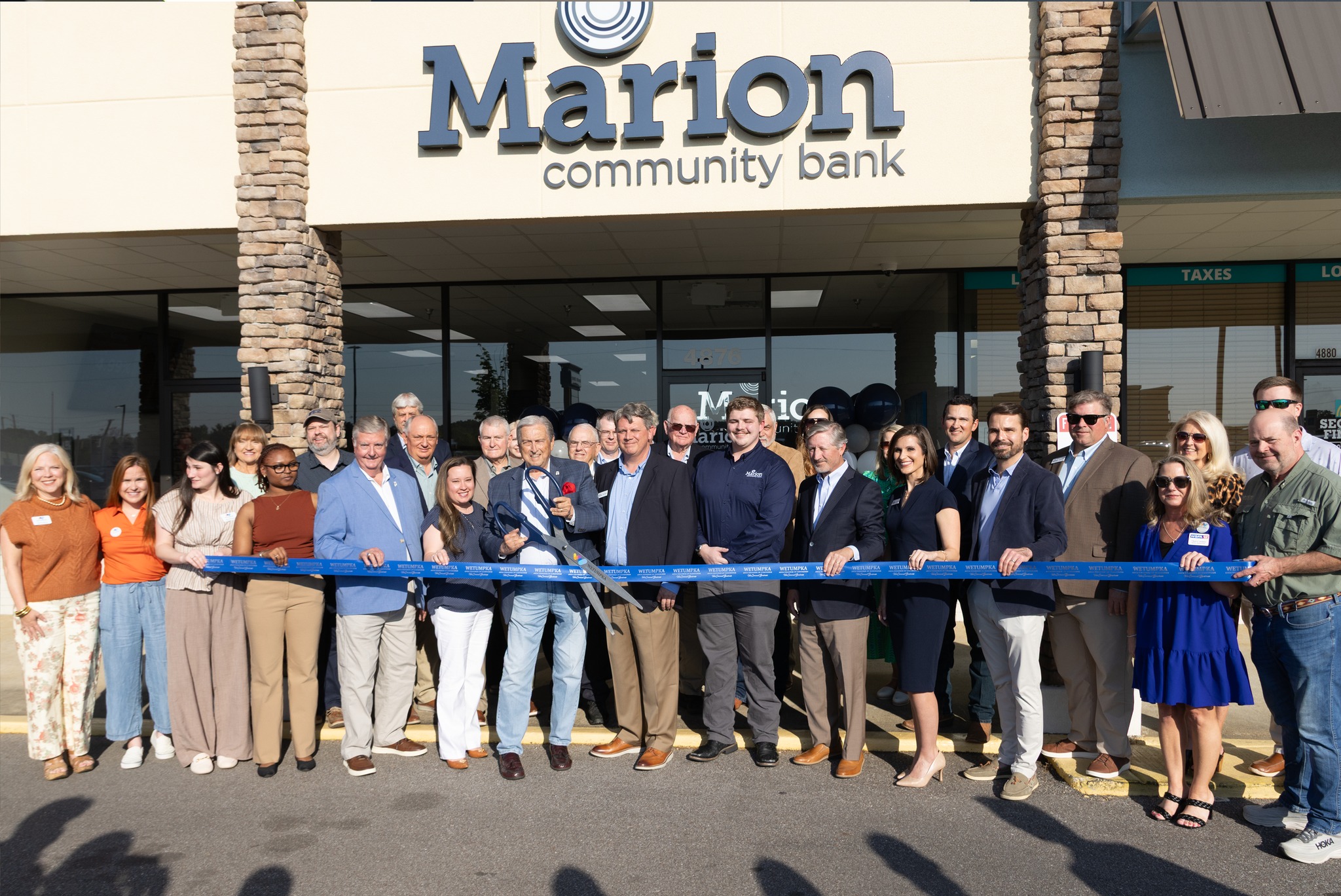 Wetumpka Ribbon Cutting. 30 people in the community form a line in front of the new location to cut the ribbon