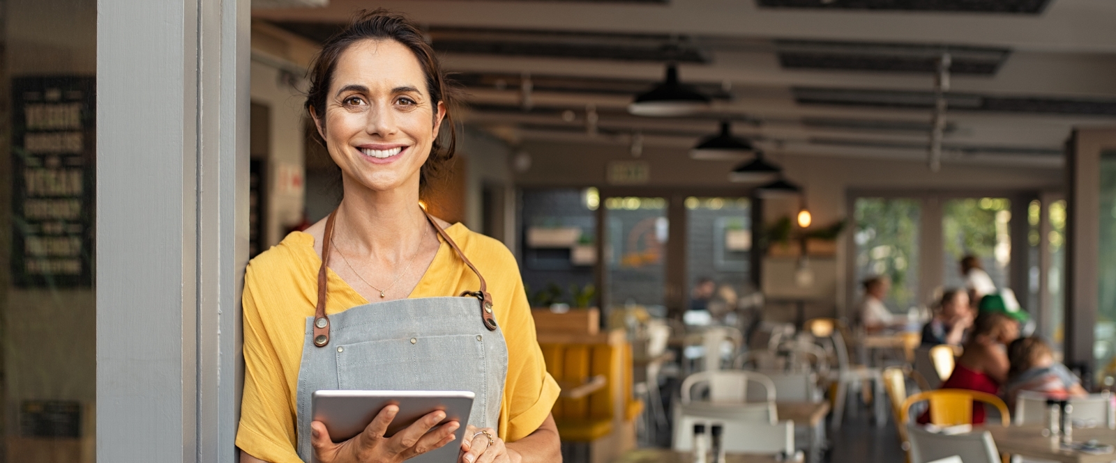 Business owner standing in front of dining area holding tablet