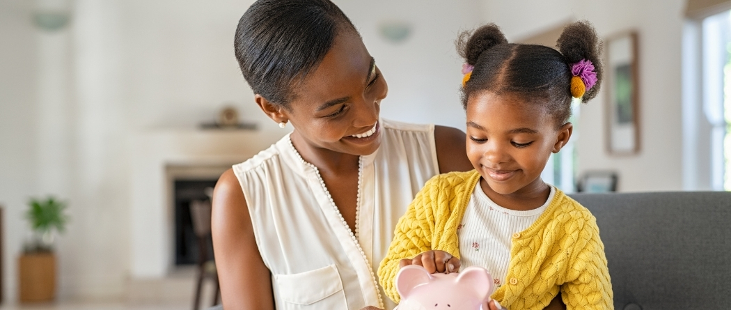 mother and daughter dropping money into piggy bank