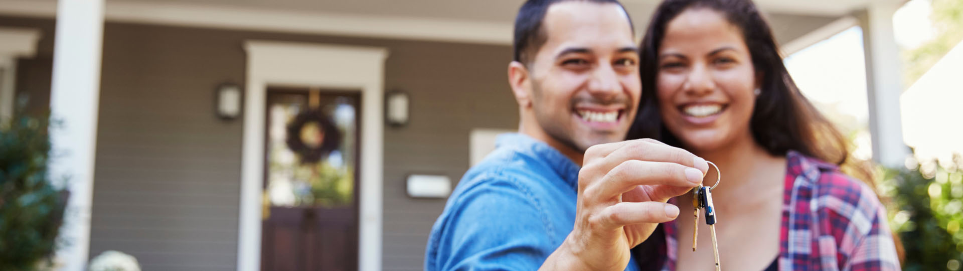 Couple smiling in front of new house holding keys.
