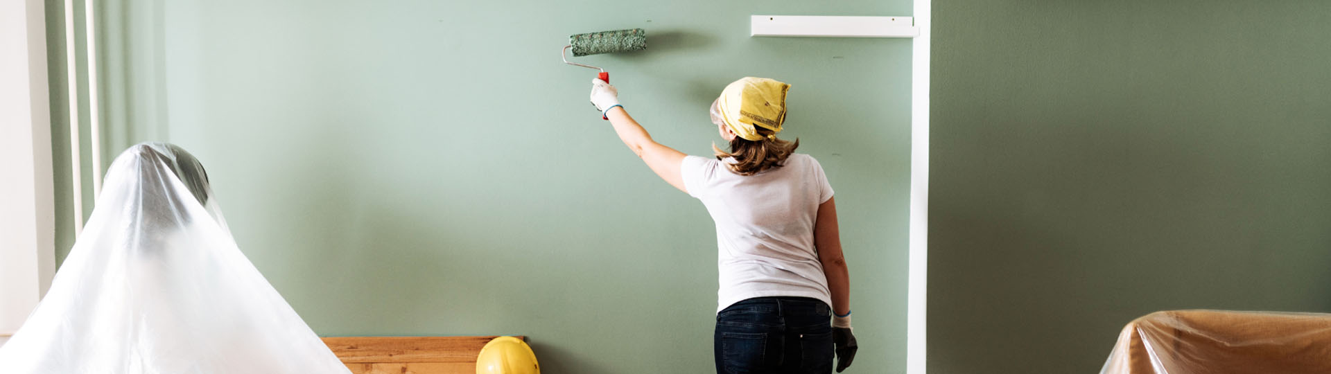 Woman painting a wall green with a roller.