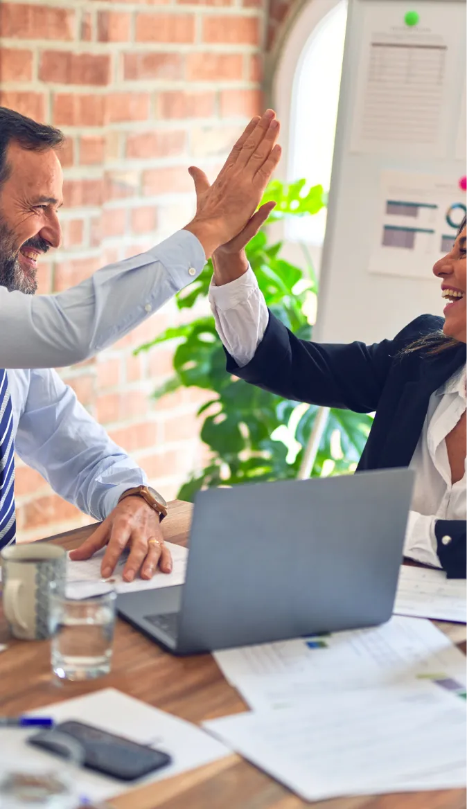 Two businesspeople high-fiving over a laptop.